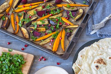 Roast vegetables on a baking tray, eggplant, carrot, baby beetroot served with parsley and pomegranate seeds with homemade tortillas.