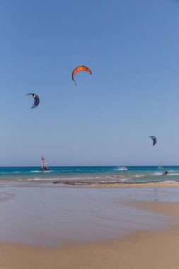 Uçurtma alıştırması yapan insanlar. Prasonisi, Rhodes yarımadasındaki plaj. Deniz kıyısında renkli uçurtmalar. Mavi deniz ve rüzgar sörfü.