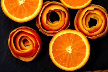 Bir mandalina bir soyma narenciye bir dekor ile koyu bir taş üzerinde servis edilir. Yarım mandalina ve bir tabakta spiral kabuğu. Close. Yumuşak odak. Üstte görüntü.
