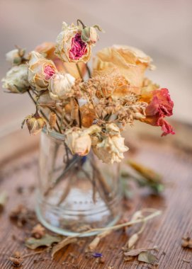 Sanat fotoğrafçılığı. Güller cam bir vazoda soldu. Ahşap bir yüzeyüzerinde soluk güller ve kuru ot. Doğa duvar kağıdı bulanık arka plan. Tonlu görüntü. Closeup. Yumuşak odaklama.