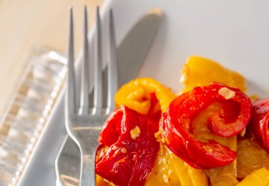 Beyaz bir tabakta pişmiş kırmızı sarı kızarmış tatlı biber. Çatal bıçak. Vejetaryen yemekleri. Yumuşak odak. Üst te. Closeup. Kopyalama alanı.