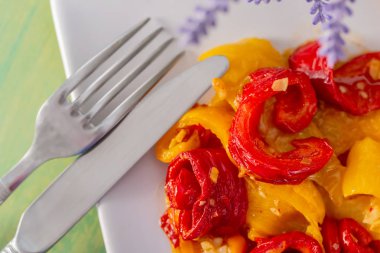 Beyaz bir tabakta pişmiş kırmızı sarı kızarmış tatlı biber. Çatal bıçak. Vejetaryen yemekleri. Yumuşak odak. Closeup. Üstte görüntü.