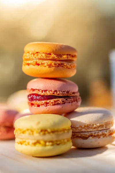 Delicious sweet airy colored french pastries. Sweets macarons in the summer evening in an orchard. Blurred background. Soft focus.