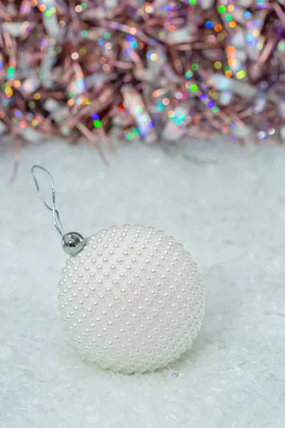 Christmas. White ball nacre pearls on a snow and beautiful blurred colorful background of glittering bokeh with glowing lights. — Stock Photo, Image