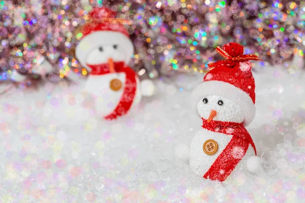 Décoration de Noël. Des bonhommes de neige avec des chapeaux rouges et des écharpes. Bonhommes de neige sur neige blanche à côté d'un fond bokeh brillant coloré . — Photo
