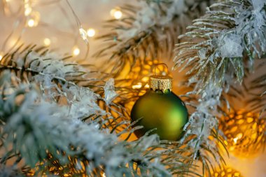 Yeni Yıl Tatili tebrik kartı. Güzel yeşil top, çam dalları ve karda bir çelenk. Bulanık sarı bokeh arka plan. Sığ alan derinliği. Mavi tonda görüntü. Kopya alanı. Noel