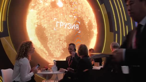 Ένας άντρας και δύο γυναίκες που κάθονται σε ένα τραπέζι και μιλούν στο τηλέφωνο κοντά στην έκθεση Spief Αγία Πετρούπολη διεθνές οικονομικό φόρουμ 2019 έκτερεν — Αρχείο Βίντεο