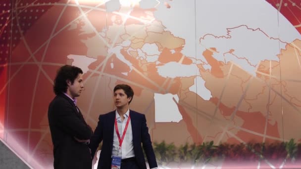 Dwóch międzynarodowych mężczyzn w garniturach dyskusji w tłumie ludzi na stoisku na wystawie Spief Sankt Petersburg International Economic forum 2019 ExpoForum — Wideo stockowe