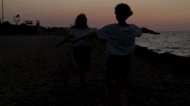 gün batımında birbirlerine doğru koşan ve denize sarılan kızların siluetleri