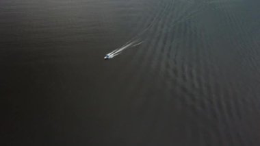 Havai üst görünümü tek başına mavi bir çatı ile beyaz küçük motorlu tekne çapraz beyaz bir iz bırakarak deniz üzerinde hızlı yelken yüzer. Havadan çekilen görüntüler