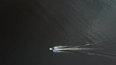 Havai üst görünümü tek başına mavi bir çatı ile beyaz küçük motorlu tekne beyaz bir iz bırakarak deniz üzerinde hızlı yelken yüzer. Havadan çekilen görüntüler