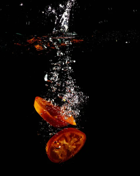 Tomato, Paprika and Eggplant slices fall into water, on black background