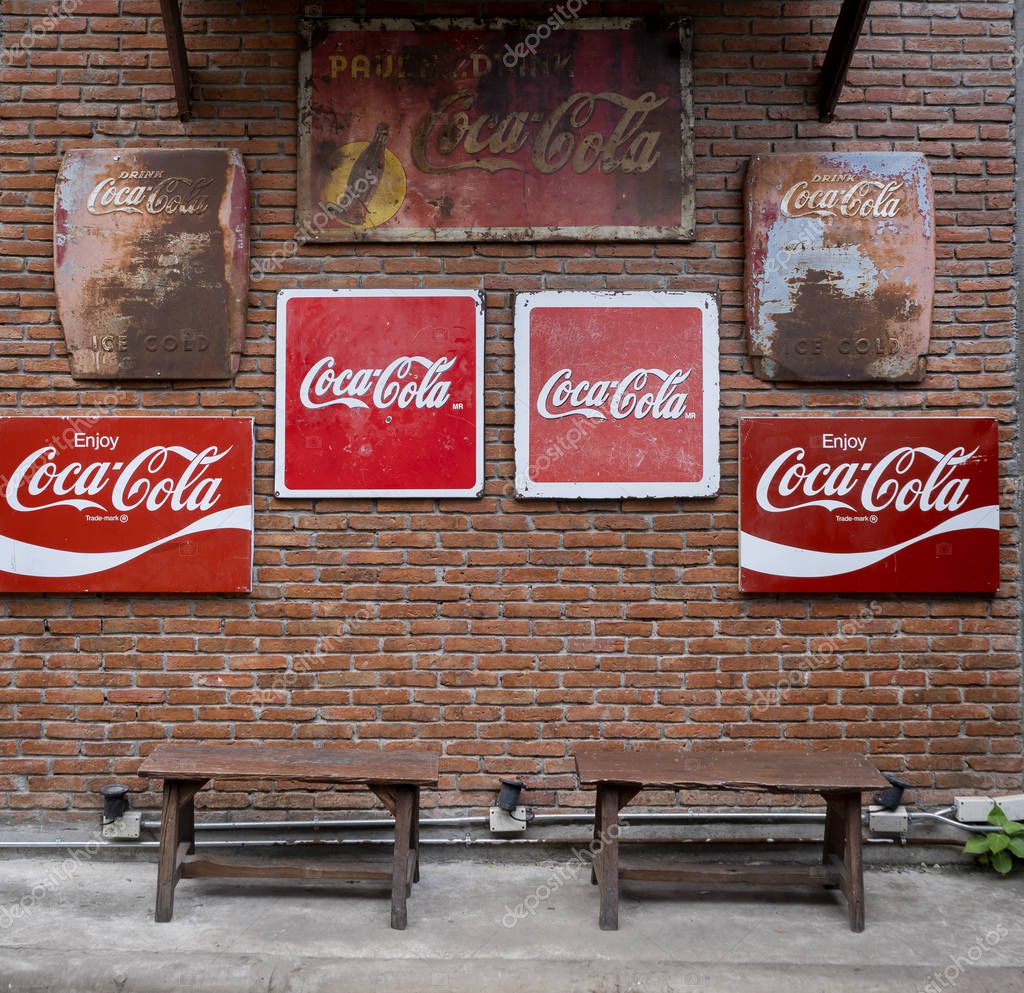 Bangkok, Thailand - June 19, 2019 : Vintage Coca Cola sign on the brick wall with wooden chairs