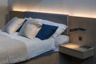 Modern beyaz, mavi, kahverengi kumaş yastıklar. Yatağın iç dekorasyonunda kahverengi kumaş başlıklı.