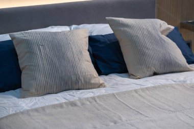 Modern beyaz, mavi, kahverengi kumaş yastıklar. Yatağın iç dekorasyonunda gri kumaş yatak başlığı var.