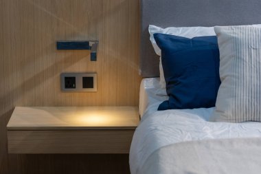 Modern beyaz, mavi, kahverengi kumaş yastıklar. Yatağın iç dekorasyonunda gri kumaş yatak başlığı var.