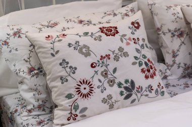 Yatağın iç dekorasyonunda güzel işlemeli çiçek desenli modern beyaz kumaş yastıklar.