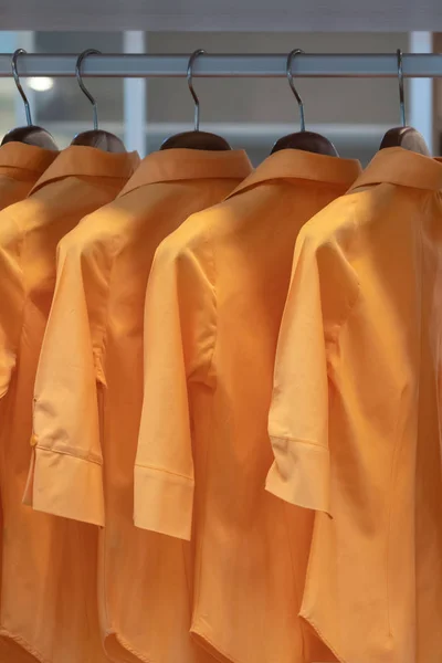 Women orange colors shirts hang in a wooden closet at modern home decoration concept interior