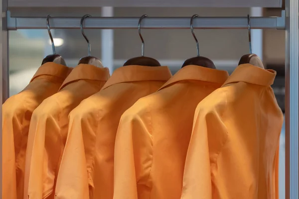Women orange colors shirts hang in a wooden closet at modern home decoration concept interior