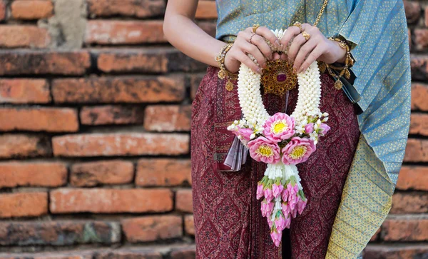 Women holding beautiful garland in here hand and wearing traditional Thai dress costume according culture with the old brick wall at the ancient temple Ayutthaya, Thailand