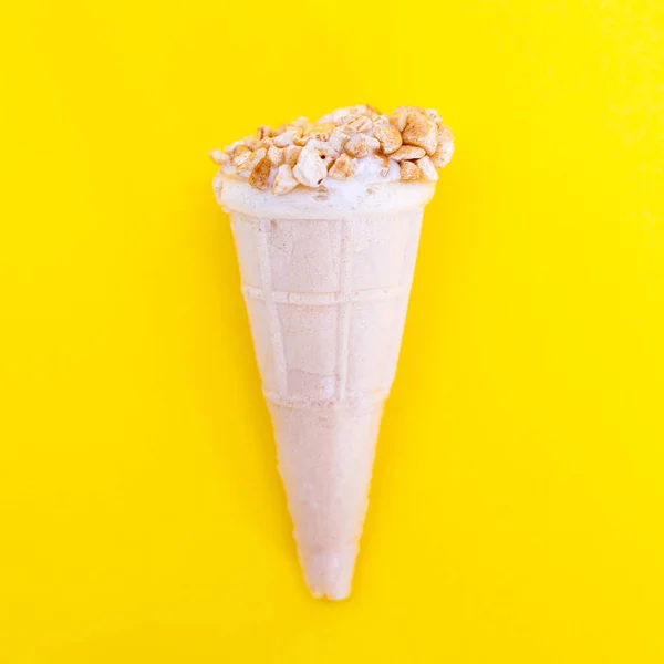 Ice cream with nuts in a waffle Cup. Waffle horn isolated on a yellow background, close-up.