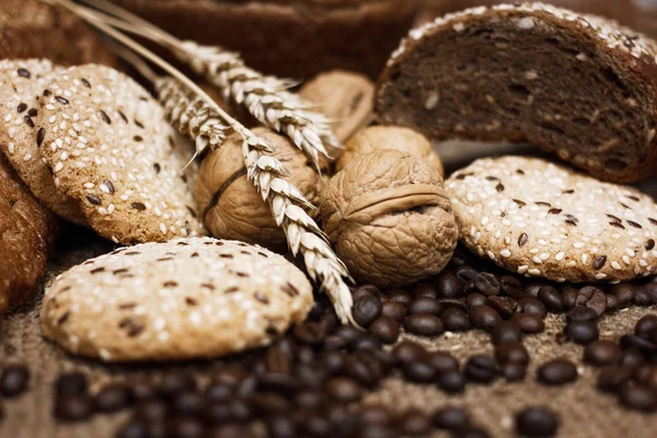 Many kinds of whole wheat bread, sesame cookies, walnuts and coffee beans and wheat spikelets are laid out on a coarse burlap. The concept of a healthy Breakfast. Image still life and selective focus.