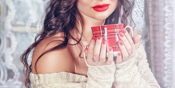 Uzun saçlı kırmızı dudakları olan bir kız ve sıcak bir içecek ile bir kupa tutan güzel bir manikür. Noel kavramı, yeni yıl, sıcak ve rahat çay.