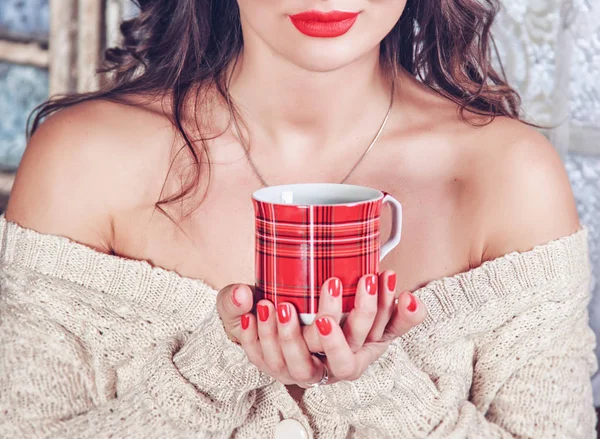 Uzun saçlı kırmızı dudakları olan bir kız ve sıcak bir içecek ile bir kupa tutan güzel bir manikür. Noel kavramı, yeni yıl, sıcak ve rahat çay.