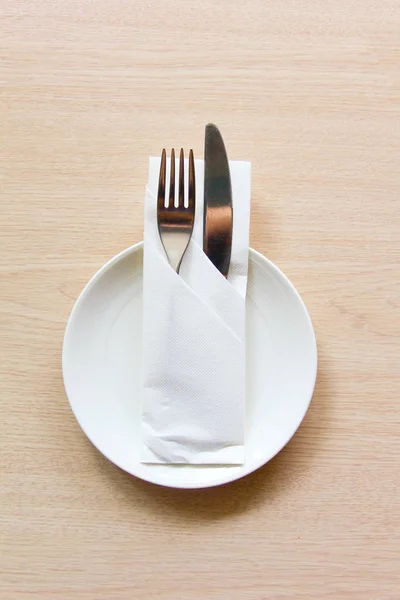 Knife and fork wrapped in a napkin lying on a white plate. The view from the top. The concept of the table setting. — Stock Photo, Image