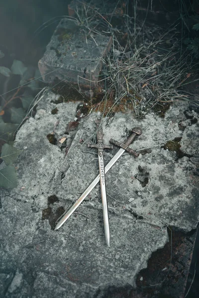 Keskin bıçaklı ve saplı iki kadim hançer eski terk edilmiş bir kalenin levhalarına çaprazlanmış. Klasik romantik arka plan kavramı.