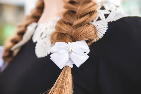 Braided hair with a white bow. A blonde girl in a strict dark school uniform with a white lace collar, close-up. Elements of strict school uniform at the graduation and the last call