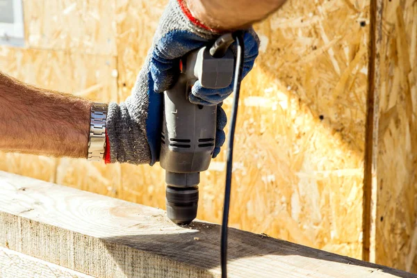 A worker drills a hole in a wooden bar with a drill on wooden. Wooden bar drilling with an electric drill. Construction background