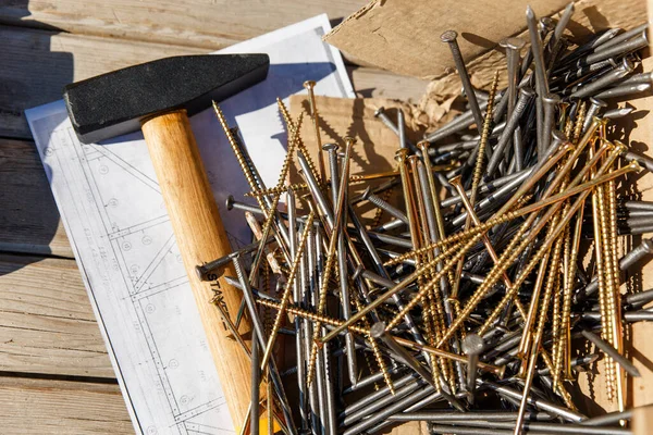 A hammer and Long nails with self-tapping screws lie on the drawing of the house construction plan. Preparation for construction. Abakan, Russia-April 6, 2020.