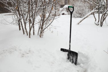 Kar küreği kış sokağının arka planında kar yığınında duruyor.