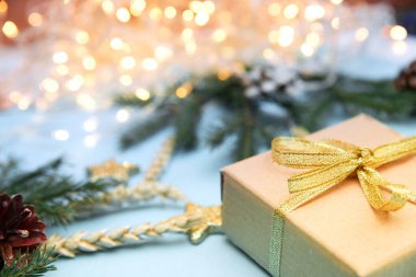 Arkaplanda parlayan çelenklerin olduğu bir Noel hediyesi kutusu. Gökyüzü mavisi arka plan ve Noel oyuncakları. Köknar dallı yeni yıl arkaplanı