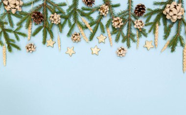 Yeşil Noel ağacı dalları ve yeni yıl oyuncakları. Gökyüzü mavisi arka planda koniler, yaylar ve altın yıldızlar. Metin için boşluk