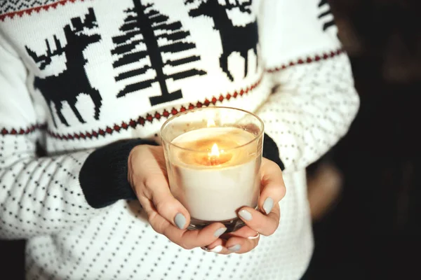 Bir kızın ellerinde yanan bir mum. Süslü ve ren geyikli bir kadın Noel mumu tutuyor.