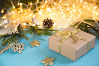 Arkaplanda parlayan çelenklerin olduğu bir Noel hediyesi kutusu. Gökyüzü mavisi arka plan ve Noel oyuncakları. Köknar dallı yeni yıl arkaplanı