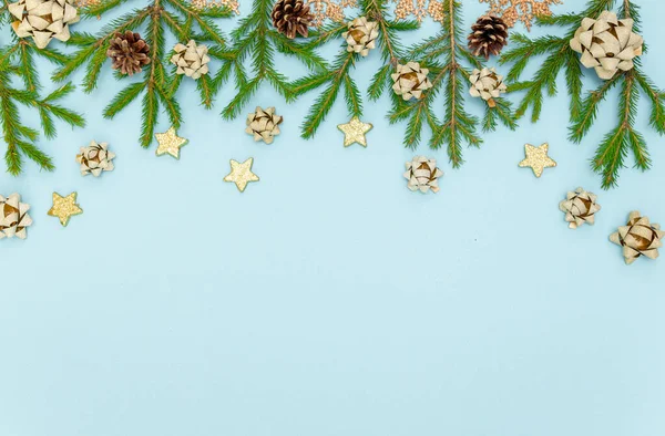 Yeşil Noel ağacı dalları ve yeni yıl oyuncakları. Gökyüzü mavisi arka planda koniler, yaylar ve altın yıldızlar. Metin için boşluk