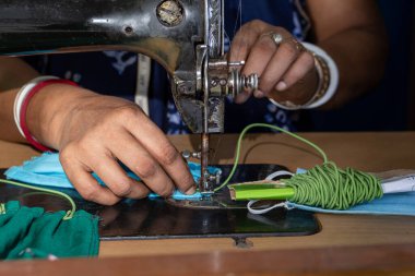 Eski dikiş makinesi üzerinde çalışan Hintli kadın - Coronavirus 'a karşı ev yapımı yüz maskeleri yapıyor veya covid19 yayılıyor, hareketli iğne ve kumaş tutan parmaklar üzerinde yakın plan detaylar.