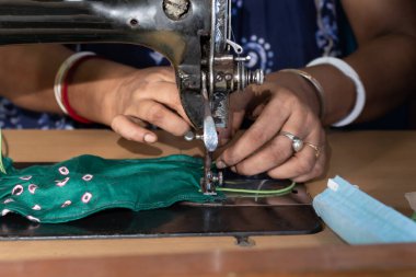 Eski dikiş makinesi üzerinde çalışan Hintli kadın - Coronavirus 'a karşı ev yapımı yüz maskeleri yapıyor veya covid19 yayılıyor, hareketli iğne ve kumaş tutan parmaklar üzerinde yakın plan detaylar.