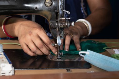 Eski dikiş makinesi üzerinde çalışan Hintli kadın - Coronavirus 'a karşı ev yapımı yüz maskeleri yapıyor veya covid19 yayılıyor, hareketli iğne ve kumaş tutan parmaklar üzerinde yakın plan detaylar.