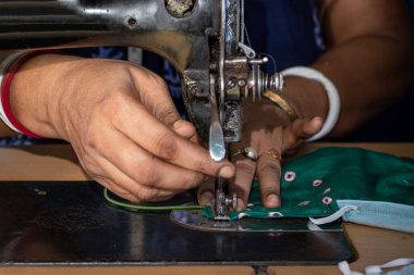 Eski dikiş makinesi üzerinde çalışan Hintli kadın - Coronavirus 'a karşı ev yapımı yüz maskeleri yapıyor veya covid19 yayılıyor, hareketli iğne ve kumaş tutan parmaklar üzerinde yakın plan detaylar.