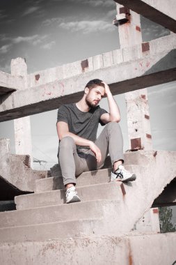 Sakallı, yakışıklı yüzlü, atletik yapılı genç bir adam. Fotoğraflar profesyoneldir.