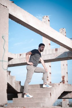 Sakallı, yakışıklı yüzlü, atletik yapılı genç bir adam. Fotoğraflar profesyoneldir.