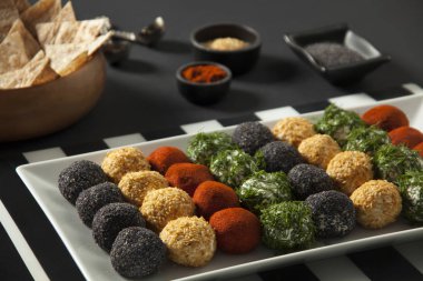 baharatlı, susam, mavi haşhaş, kırmızı biber, maydanoz peynir topları meze ve kepekli cips ile peynir tabağı yakın