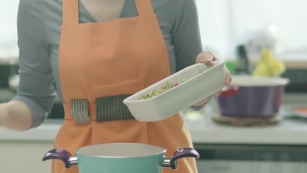 台所で準備中に鍋に食材を入れる女性のトリミングビュー — ストック動画