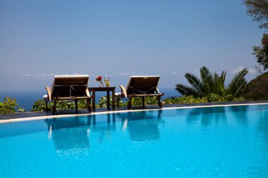 Yaz ve tatil konsepti. Bir bardak kokteyl ve renkli çiçekler. Güneş yatağı, yüzme havuzu ve harika bir deniz manzarası.