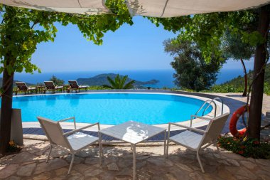 Bahçede yüzme havuzu ve ağaçlı güzel dağ manzarası. Yüzme havuzunun yanında masa ve sandalyeler..