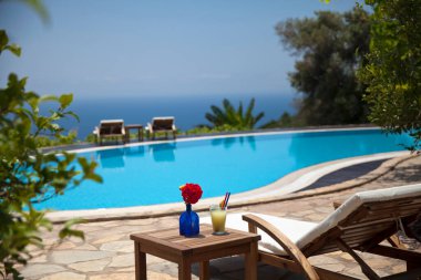 Harika bir bahçede deniz manzaralı bir yüzme havuzu. Kırmızı yaz çiçeği, portakal suyu ve iskemle. Yaz ve tatil konsepti